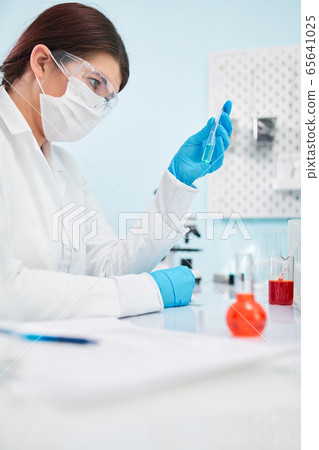 Close up of woman laboratory technician in blue rubber gloves holding test tube. 65641025