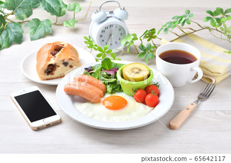 Image of one plate breakfast (Western food, fried egg, sausage). Raisin bread, coffee, smartphone and clock. Image of one plate breakfast (Western food, fried egg, sausage). Raisin bread, coffee, smartphone and clock. 65642117