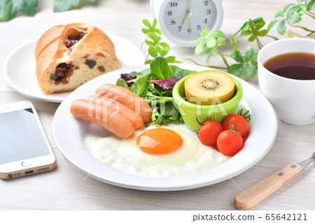 Image of one plate breakfast (Western food, fried egg, sausage). Raisin bread, coffee, smartphone and clock. Image of one plate breakfast (Western food, fried egg, sausage). Raisin bread, coffee, smartphone and clock. 65642121
