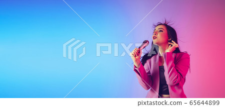 Caucasian female singer portrait isolated on gradient studio background in neon light, flyer with copyspace for ad Caucasian female singer portrait isolated on gradient studio background in neon light, flyer with copyspace for ad 65644899