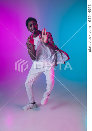 African-american male singer portrait isolated on gradient studio background in neon light African-american male singer portrait isolated on gradient studio background in neon light 65644968