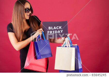 Black Friday. Woman with the inscription Black Friday and gift bags on a red background Black Friday. Woman with the inscription Black Friday and gift bags on a red background 65645245