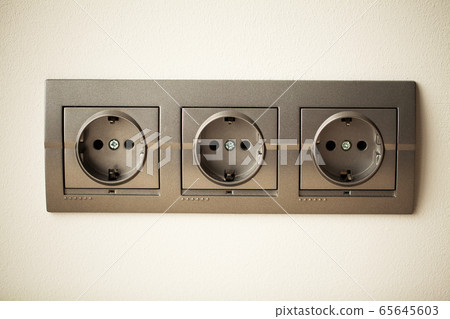 Closeup view of a group of gray european electrical outlets located on a gray wall Closeup view of a group of gray european electrical outlets located on a gray wall 65645603