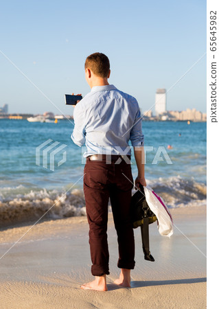 A man in casual wear on the beach with a phone. 65645982