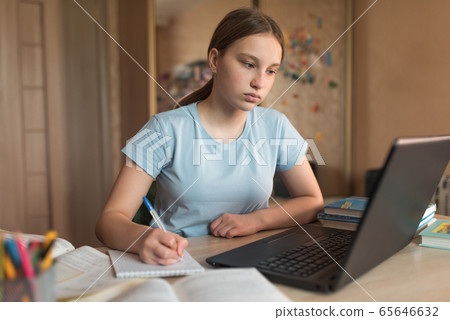 Concentrated girl teenager 12-14 years old, home, laptop lessons, notebook writes pen. E-education distance learning Internet and video communications. Accomplishment of lessons and test of exam. 65646632