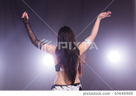 Young woman dancing in Tribal Fusion style. Belly dance on the stage. Back view. Young woman dancing in Tribal Fusion style. Belly dance on the stage. Back view. 65646989