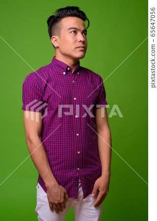Young multi-ethnic man wearing purple shirt against green background Young multi-ethnic man wearing purple shirt against green background 65647056
