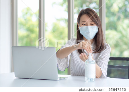 Business woman wearing mask and using personal sanitizer to cleaning her hand in office 65647250