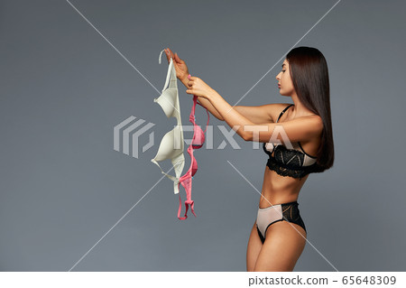 A difficult choice, a beautiful girl chooses a bra, holding bras of different colors in her hands. Gray background, copy space, make difficult choices. A difficult choice, a beautiful girl chooses a bra, holding bras of different colors in her hands. Gray background, copy space, make difficult choices. 65648309