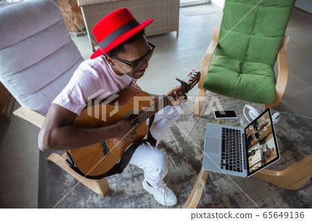 African-american musician playing guitar during online concert at home isolated and quarantined, impressive improvising 65649136