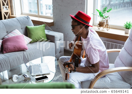 African-american musician playing guitar during online concert at home isolated and quarantined, impressive improvising 65649141