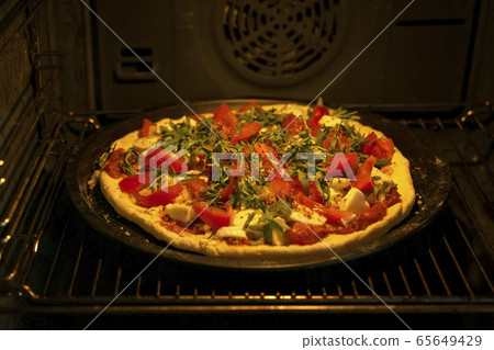 Homemade pizza with fresh tomatoes, mozzarella and arugula in oven, open door, dark background, selective focus, real lifestile Homemade pizza with fresh tomatoes, mozzarella and arugula in oven, open door, dark background, selective focus, real lifestile 65649429