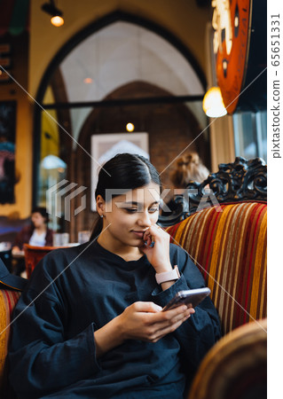 Pretty young girl resting on a big soft chair in a cafe, chatting on the phone Pretty young girl resting on a big soft chair in a cafe, chatting on the phone 65651331