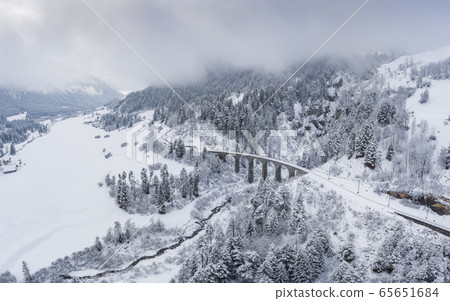 Aerial View of the Landwasser Viaduct with Railway without famous train at winter, landmark of Switzerland, snowing, river and mountains 65651684