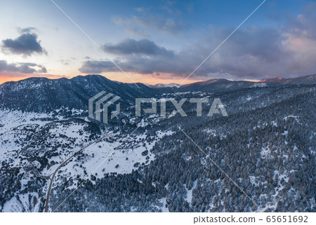 The Aerial view of a sunset over mountain in Arahova, Greece, a view of the valley below with trees covered by snow, colors of sunset The Aerial view of a sunset over mountain in Arahova, Greece, a view of the valley below with trees covered by snow, colors of sunset 65651692