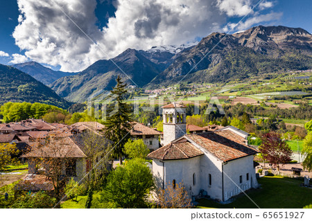 Aerial view of valley with church in Cares, Trentino, green slopes of the mountains of Italy, huge clouds over a valley, roof tops of houses, Dolomites on background 65651927