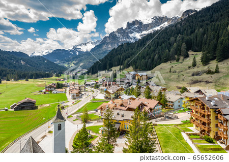 Aerial view of valley with Chalet, green slopes of the mountains of Italy, Trentino, Fontanazzo, huge clouds over a valley, roofs of houses of settlements, green meadows, Dolomites on background, 65652606
