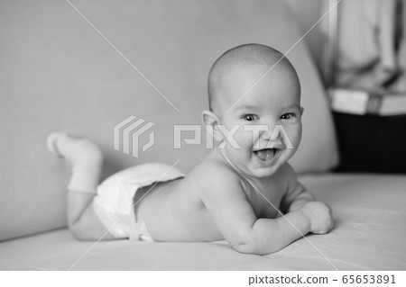 Black and white portrait of little smiling newborn baby. Cute happy baby lying on stomach and laughing, closeup 65653891