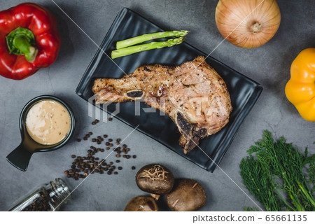 Top view of grilled pork steak surrounded by organic vegetable ingredients. 65661135