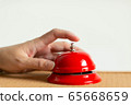 Close-up of index finger pressing the bell button of red vintage style handbell on wooden table. 65668659
