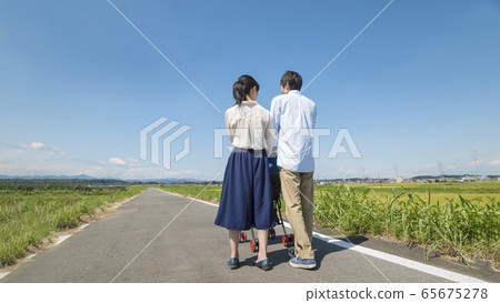 Rear view of a young couple holding a stroller in nature and taking a walk Rear view of a young couple holding a stroller in nature and taking a walk 65675278