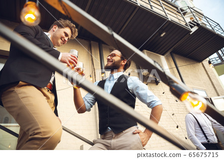 Two men talking, celebrating, look happy, have corporate party at office or bar Two men talking, celebrating, look happy, have corporate party at office or bar 65675715