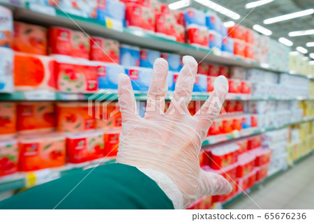 while shopping, a buyer in a supermarket carries a cart with goods with a hand in plastic glove because of the threat of a bacterial or viral infection while shopping, a buyer in a supermarket carries a cart with goods with a hand in plastic glove because of the threat of a bacterial or viral infection 65676236