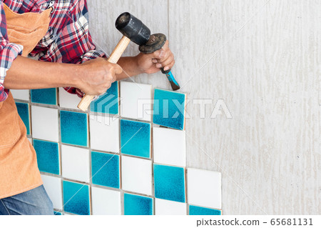 Contract worker using hammer and gouge to chisel or carve the tile from the wall for fixing wall. 65681131