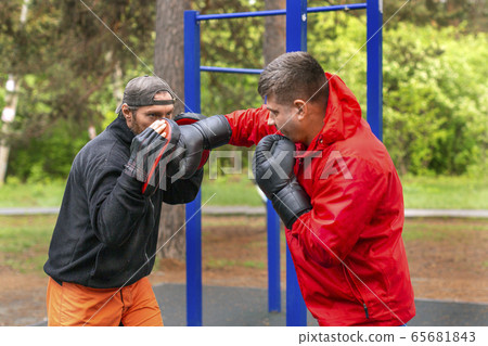 Middle-aged boxer training with coach outdoors Middle-aged boxer training with coach outdoors 65681843