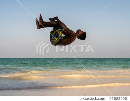 Young Attractive Muscular and Strong Athletic Black African Man at the White Sand Beach Training Acrobatics and Jumping Gymnastics Beach Performance 65682996