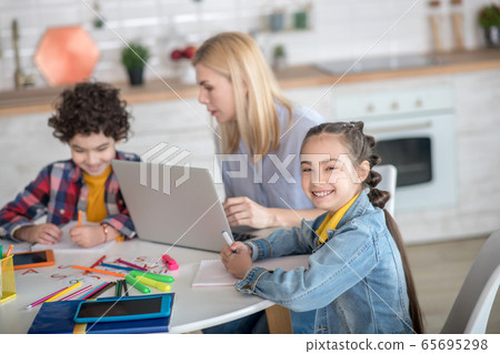 Curly boy and dark-haired girl sitting at table, blonde female sitting between them with laptop 65695298