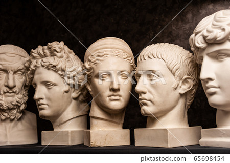 Group gypsum busts of ancient statues human heads for artists on a dark background. Plaster sculptures of antique people faces. Renaissance epoch style. Academic subject. Blank for creativity. 65698454