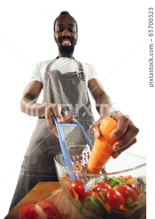 Amazing african-american man preparing unbelievable food with close up action, details and bright emotions, professional cook. Cutting carrot to salad Amazing african-american man preparing unbelievable food with close up action, details and bright emotions, professional cook. Cutting carrot to salad 65700323