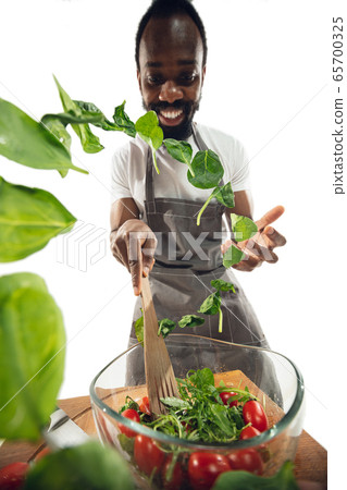 Amazing african-american man preparing unbelievable food with close up action, details and bright emotions, professional cook. Adding salad greens on the fly Amazing african-american man preparing unbelievable food with close up action, details and bright emotions, professional cook. Adding salad greens on the fly 65700325