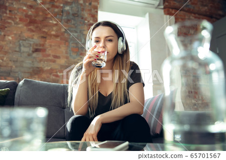 Young woman wearing wireless headphones gesturing during a video conference in the living room. Attented listening Young woman wearing wireless headphones gesturing during a video conference in the living room. Attented listening 65701567