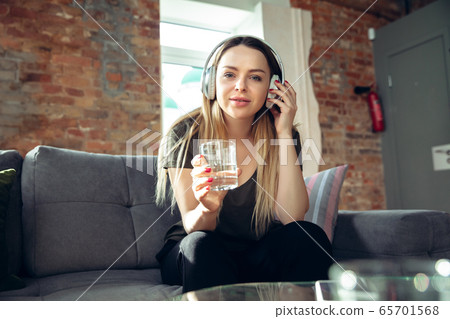 Young woman wearing wireless headphones gesturing during a video conference in the living room. Attented listening Young woman wearing wireless headphones gesturing during a video conference in the living room. Attented listening 65701568