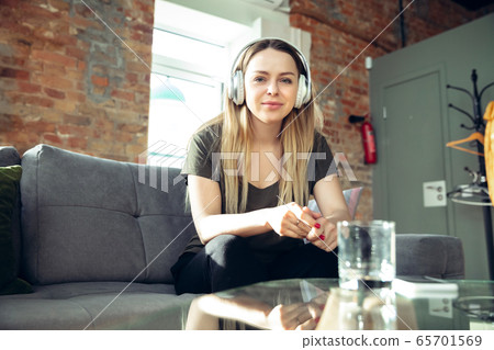Young woman wearing wireless headphones gesturing during a video conference in the living room. Attented listening Young woman wearing wireless headphones gesturing during a video conference in the living room. Attented listening 65701569