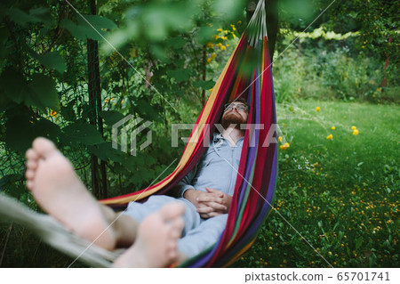 Handsome bearded man relaxing in hammock in shade Handsome bearded man relaxing in hammock in shade 65701741