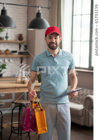 Delivery person in a red hat holding the boxes and shopping bags in his hands Delivery person in a red hat holding the boxes and shopping bags in his hands 65703239