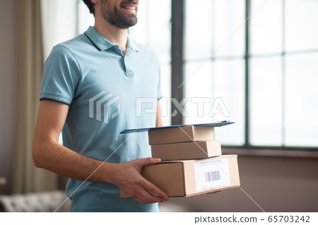 Delivery person standing in the kitchen and holding the boxes in his hands 65703242