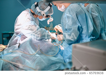 A surgeon with gloves is operating on his nose. Rhinoplasty, close-up operation. Blue light, teamwork, health, beauty. 65703638