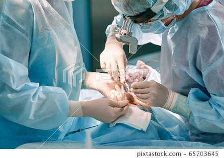 A surgeon with gloves is operating on his nose. Rhinoplasty, close-up operation. Blue light, teamwork, health, beauty. 65703645