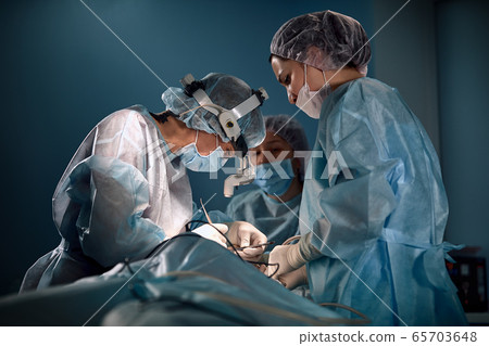 Team of women surgeons in the operating room. A modern team of doctors during an ancological operation. Fight against cancer. Reconstructive plastic surgery after cancer Team of women surgeons in the operating room. A modern team of doctors during an ancological operation. Fight against cancer. Reconstructive plastic surgery after cancer 65703648