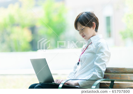坐在長椅上，經營一台筆記本電腦的女商人 65707800
