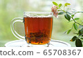 Pouring the tea with leaves of currant, lemon balm, mint, raspberry in a glass cup.Tea party outdoors 65708367