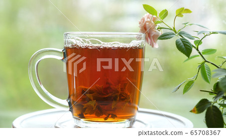 Pouring the tea with leaves of currant, lemon balm, mint, raspberry in a glass cup.Tea party outdoors 65708367
