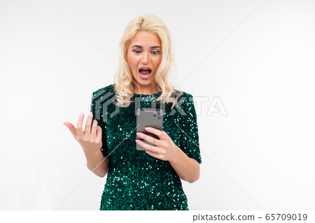 indignant woman in a shiny green dress looks at the phone screen on a white background with copy indignant woman in a shiny green dress looks at the phone screen on a white background with copy 65709019