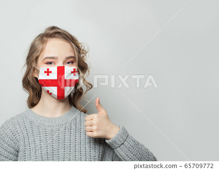 Happy woman in face mask holding thumb up  65709772