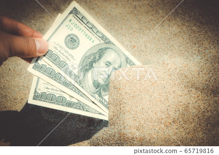 A girl takes out from the sand money notes of three hundred dollars. 65719816