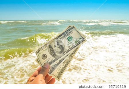 Girl holding a money bill of 300 dollars on background of sea waves Girl holding a money bill of 300 dollars on background of sea waves 65719819